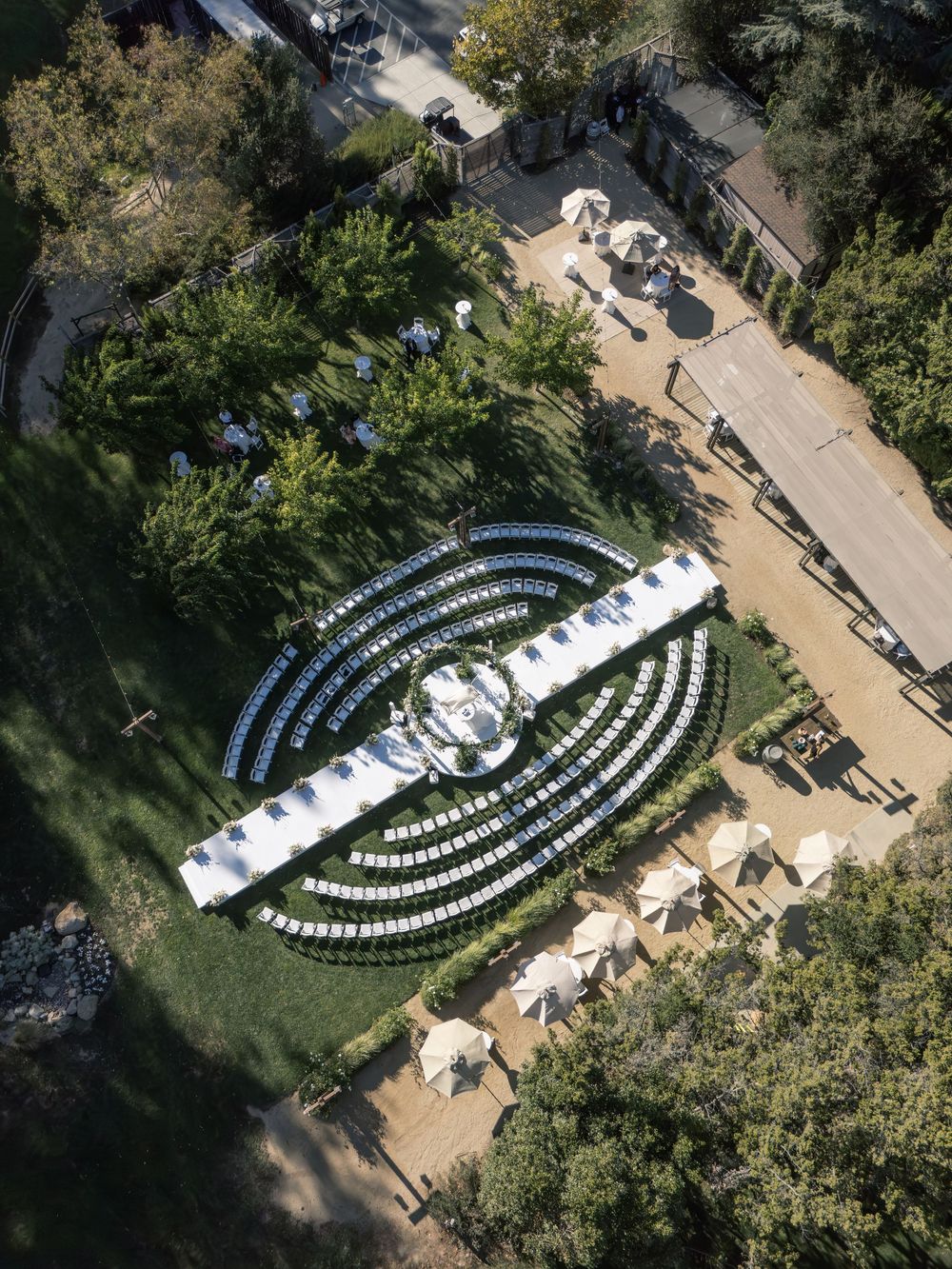 Aerial view of an elegant outdoor wedding ceremony setup with curved rows of white chairs arranged in a semicircle on green lawn.