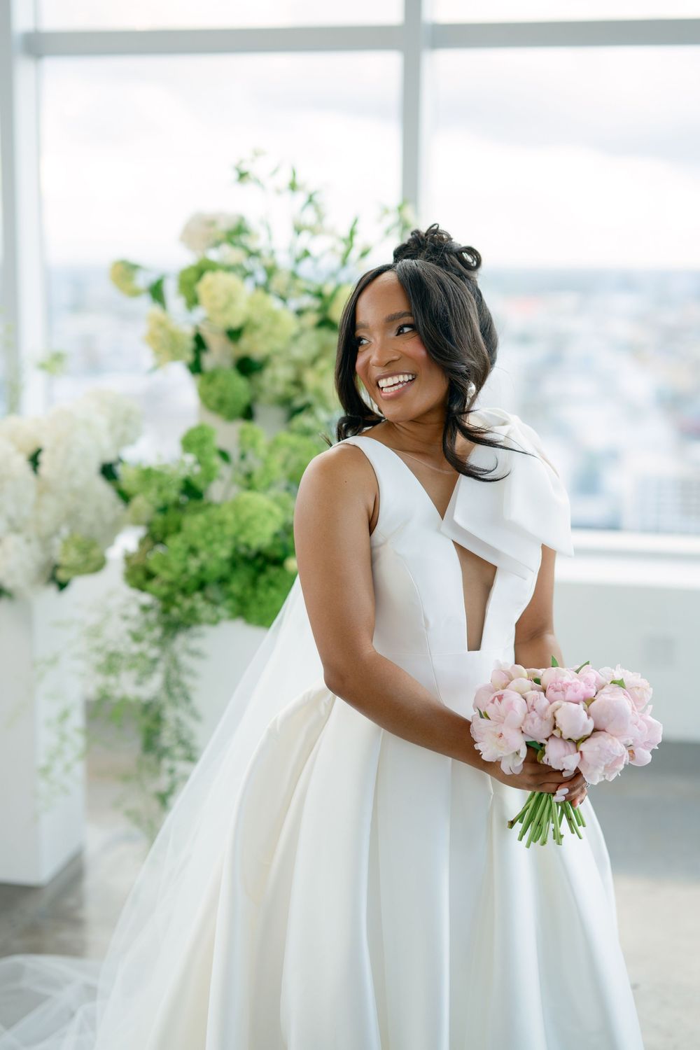Elegant bride in a white wedding gown holding pink roses in a modern bright venue.
