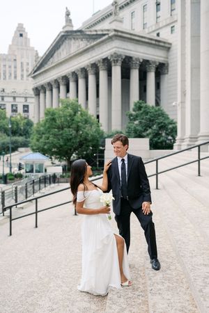 Bride and groom walking up steps outside a neoclassical building, bride holding white bouquet in elegant white gown.