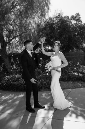 A couple shares a playful dance pose in black and white under a willow tree on their wedding day.