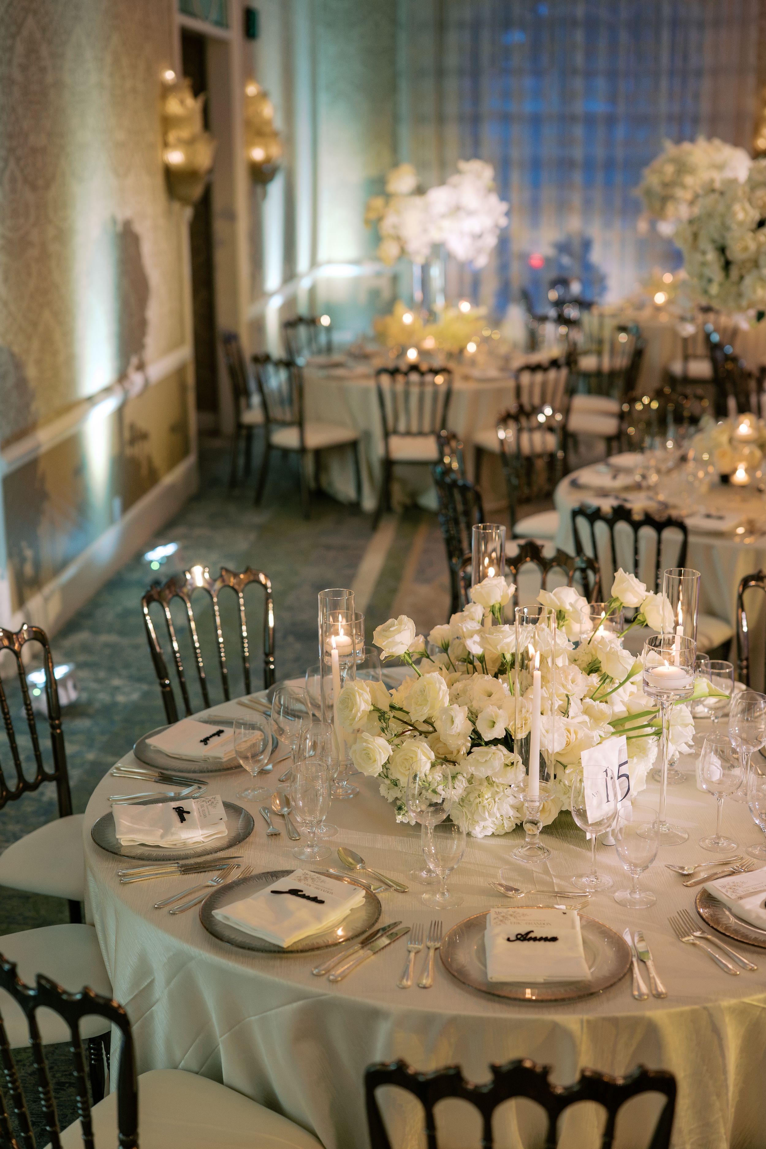 Elegant wedding reception with white floral centerpieces, candlelight, and formal table settings in a grand ballroom.