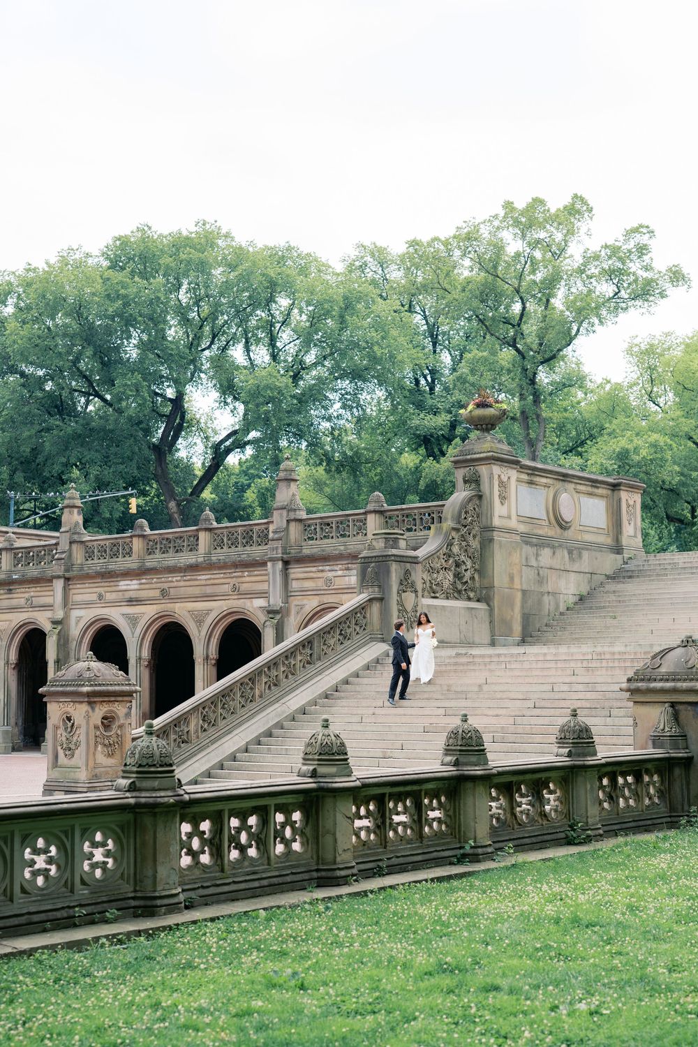 Couple in wedding attire poses on ornate stone staircase at Bethesda Terrace in Central Park, NYC.