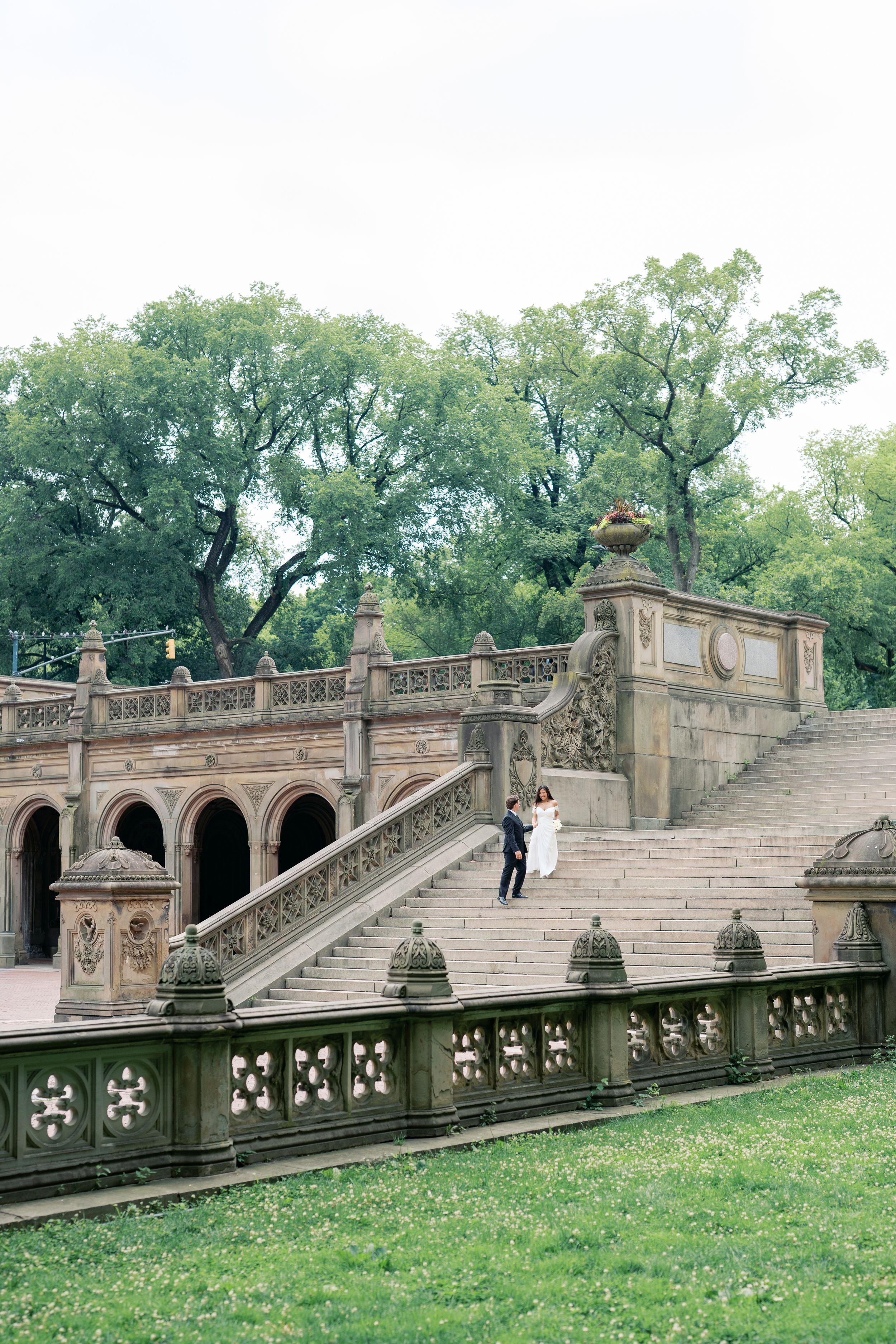 Couple in wedding attire poses on ornate stone staircase at Bethesda Terrace in Central Park, NYC.