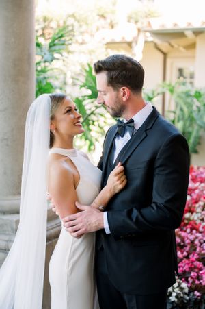 Romantic wedding portrait under garden archway with blooming pink flowers.
