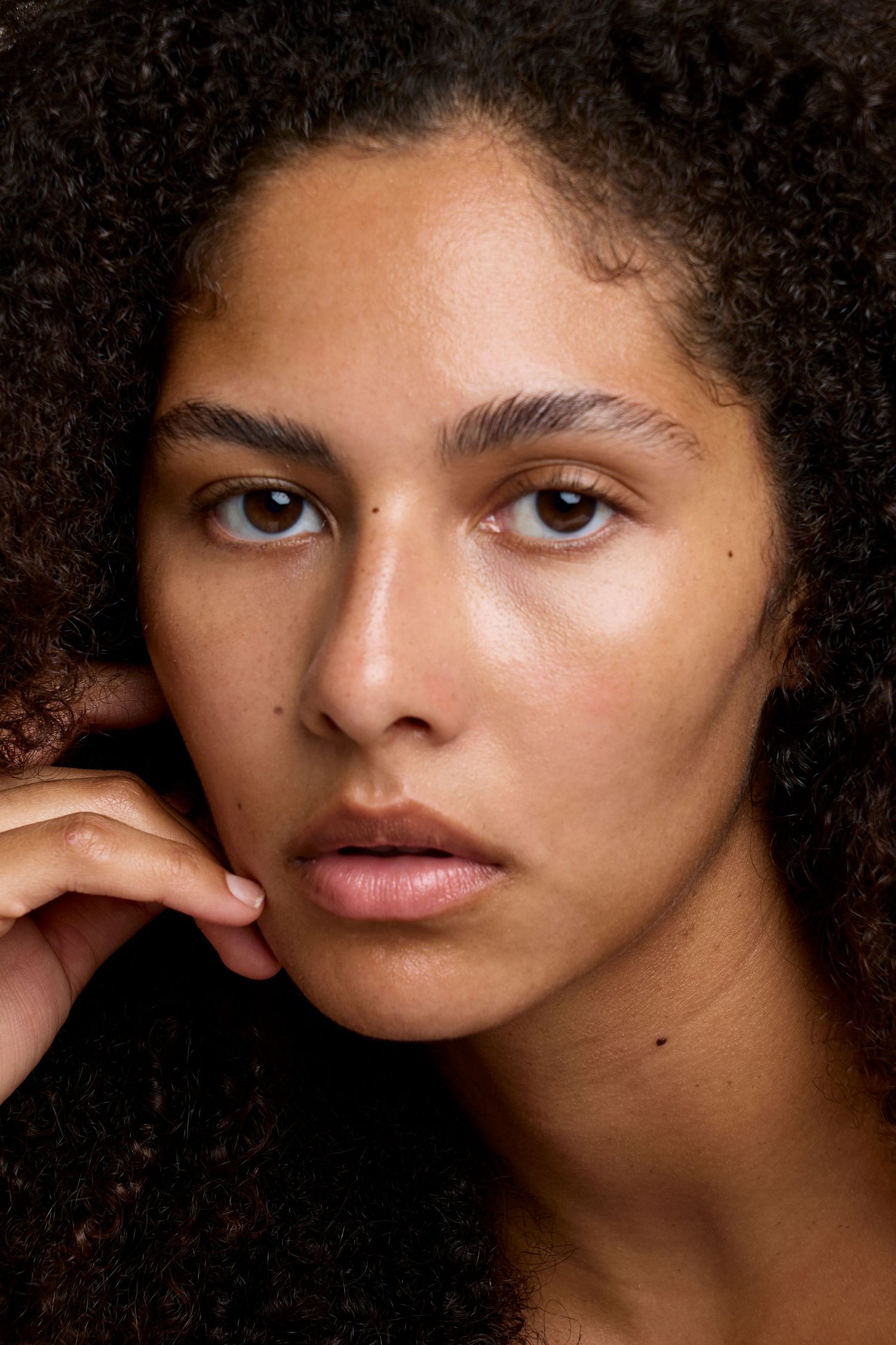 Close-up beauty portraits of someone with natural afro hair and glowing skin from different artistic angles.