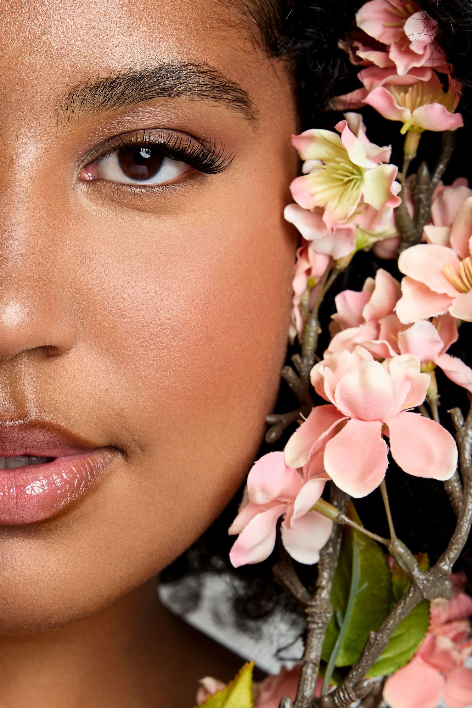 Close-up beauty shot with pink blossoms and natural makeup against dark background.