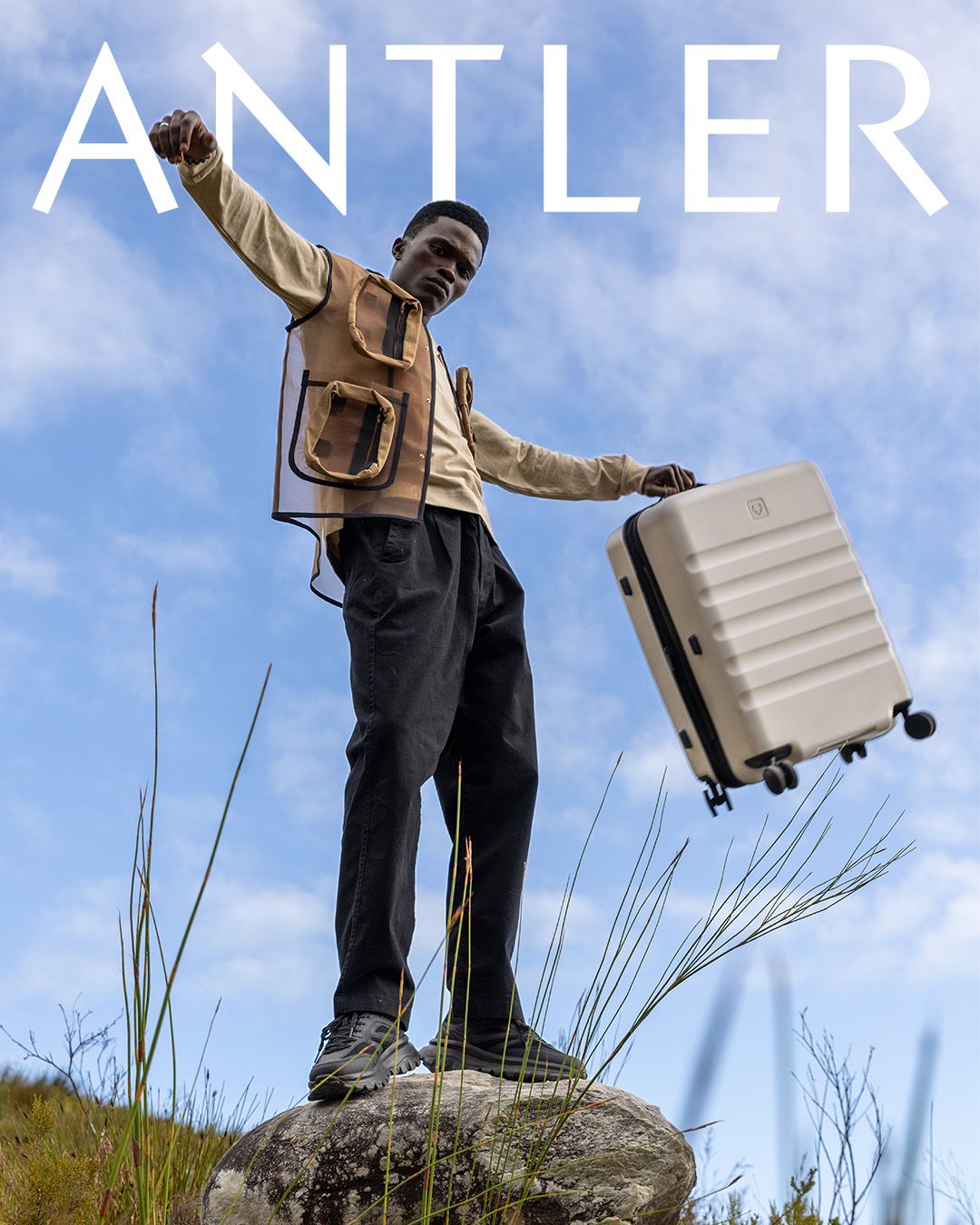 Brand photo showing traveler posing triumphantly with suitcase against blue sky.