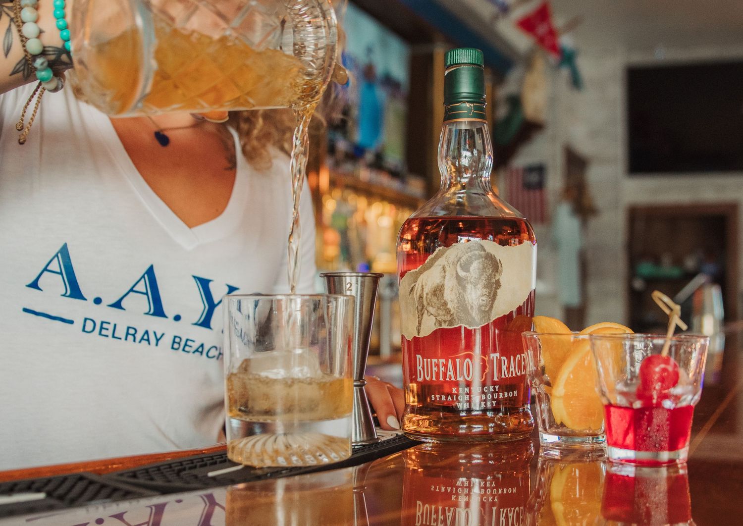 Bartender preparing cocktails at a bar with Southern Belle whiskey bottle and glassware.