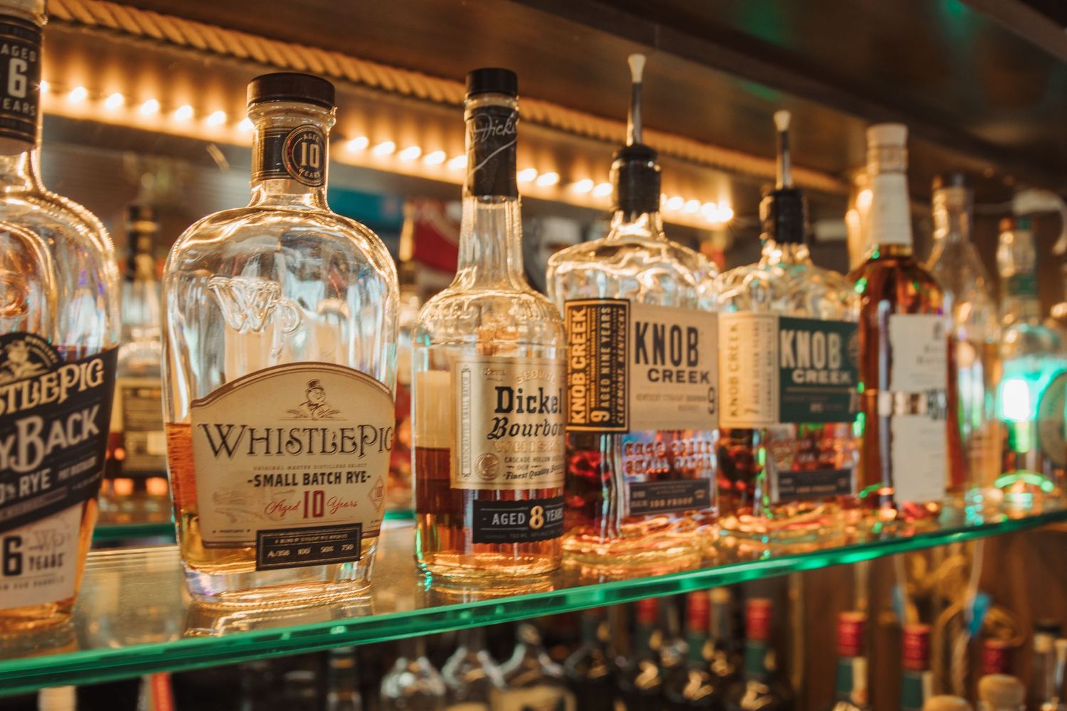 Illuminated bar shelf displaying various whiskey and spirits bottles.
