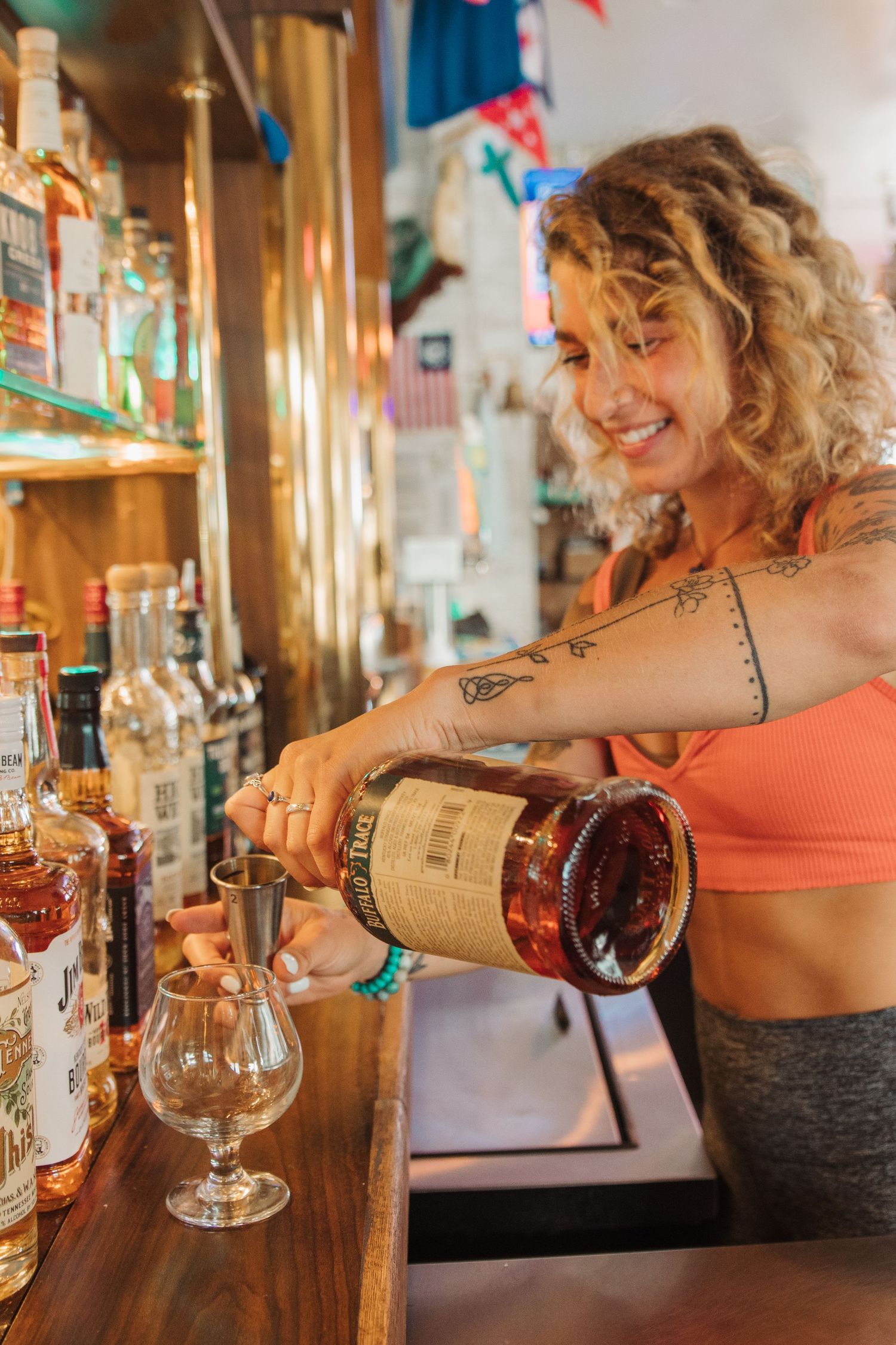 Bartender pouring a spirit into a cocktail glass at a well-stocked bar.
