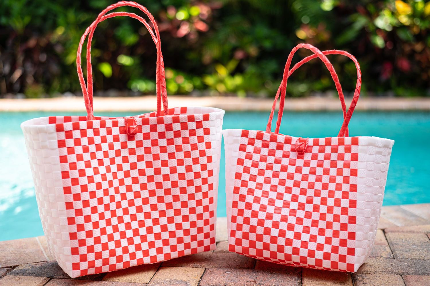 Two red and white checkered woven market bags displayed by a swimming pool.