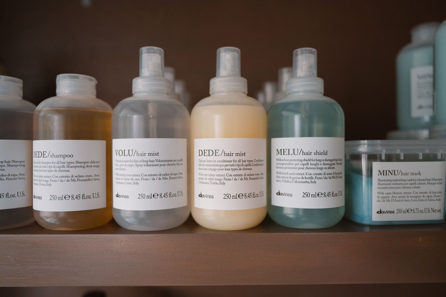 Collection of hair care products in minimalist bottles with text labels on wooden shelf.
