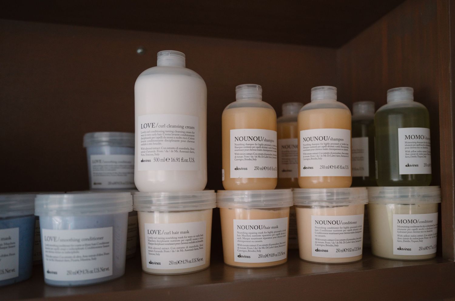Professional hair care products arranged on white shelves with pastel colored bottles.