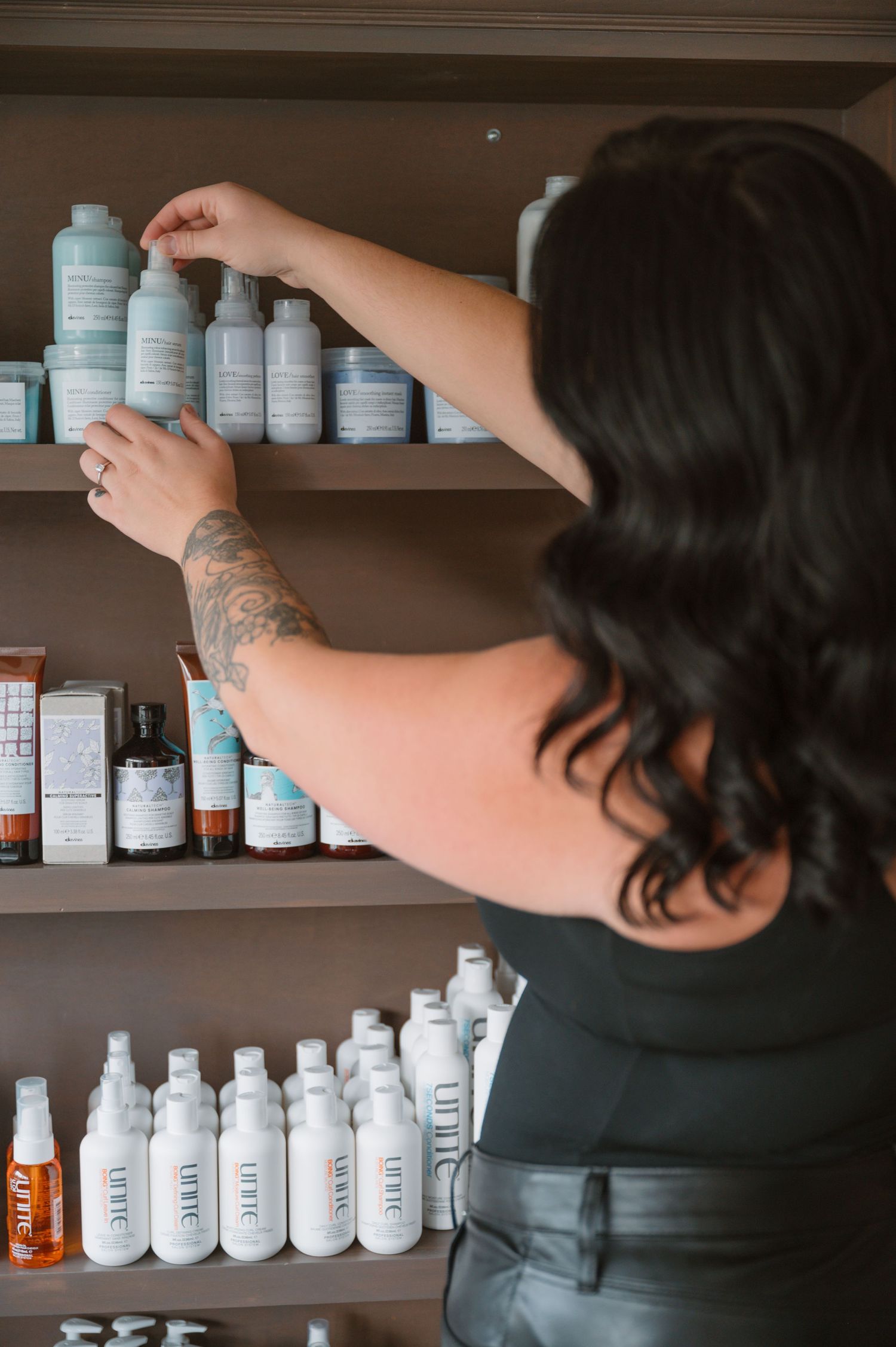 Stylist arranging bottles of Unite hair products on wooden display shelves.
