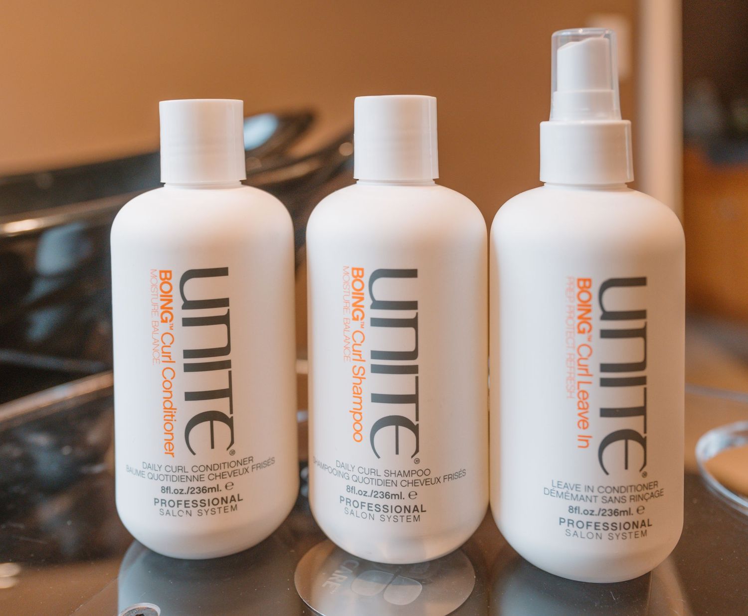 Three Unite professional haircare product bottles arranged on reflective surface.