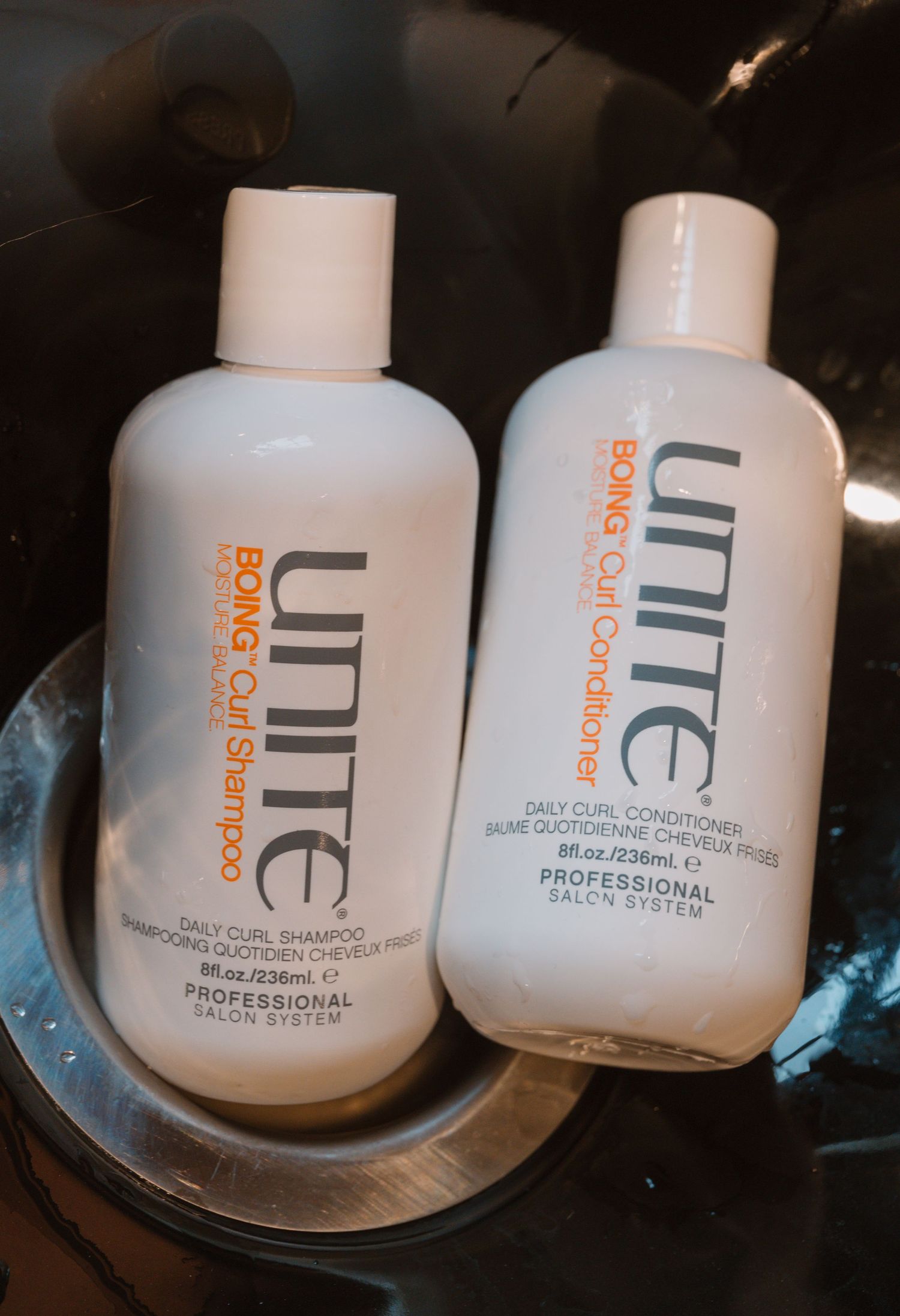 Two Unite brand shampoo and conditioner bottles displayed on glass plate.