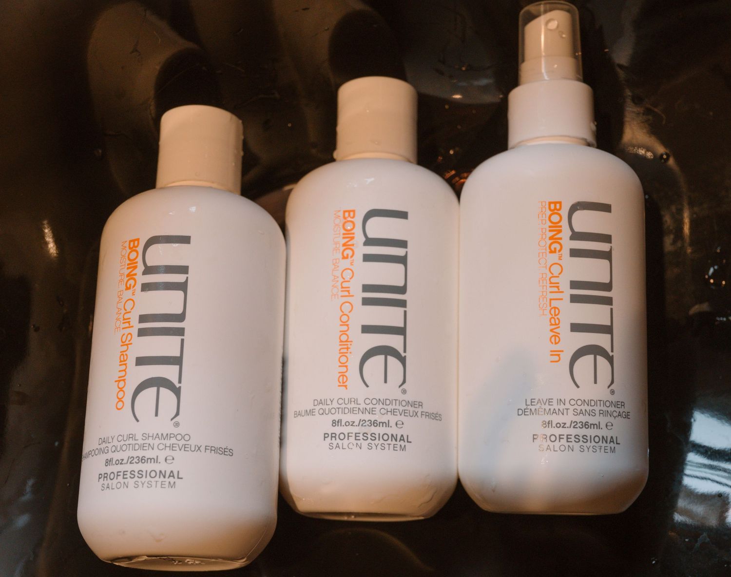 Three white Unite professional hair product bottles arranged against dark background.