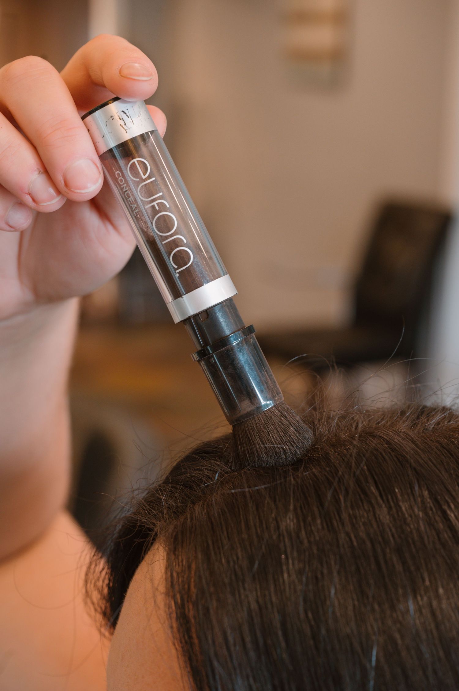 Hand applying hair product with applicator bottle to scalp during treatment.