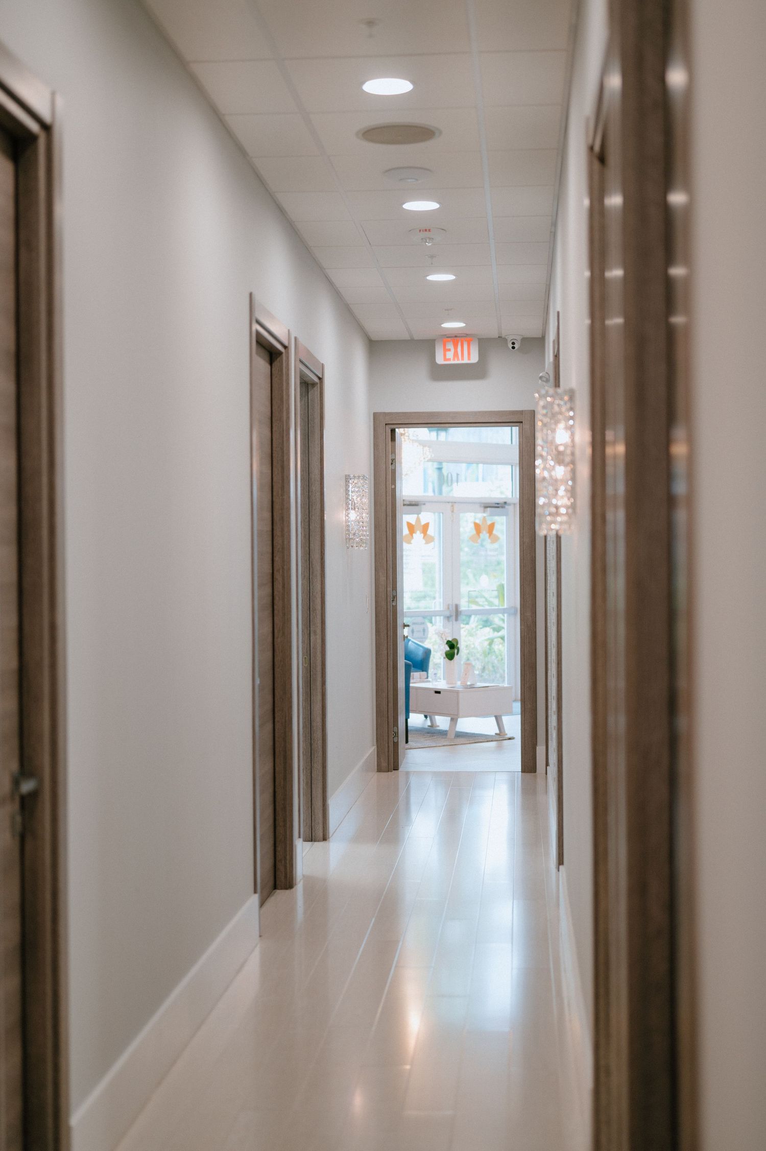 Long bright corridor with crystal sconces and modern decor leading to a window.