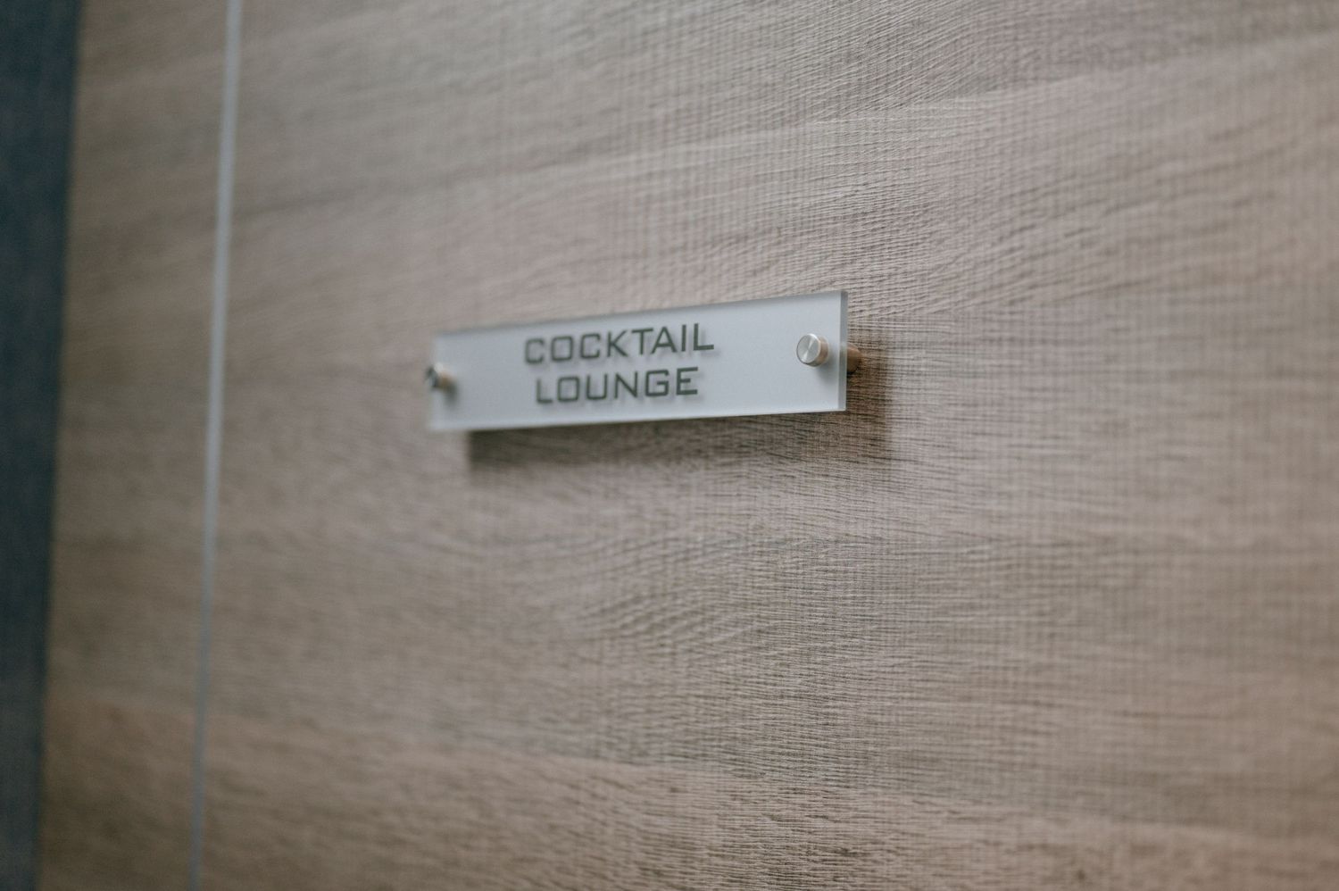 Close-up of a Cocktail Lounge room label mounted on a beige wall.