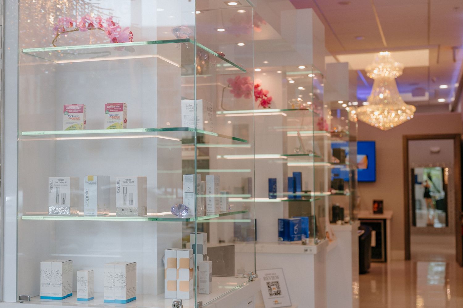 Glass shelves displaying skincare products with crystal chandelier and pink accents.
