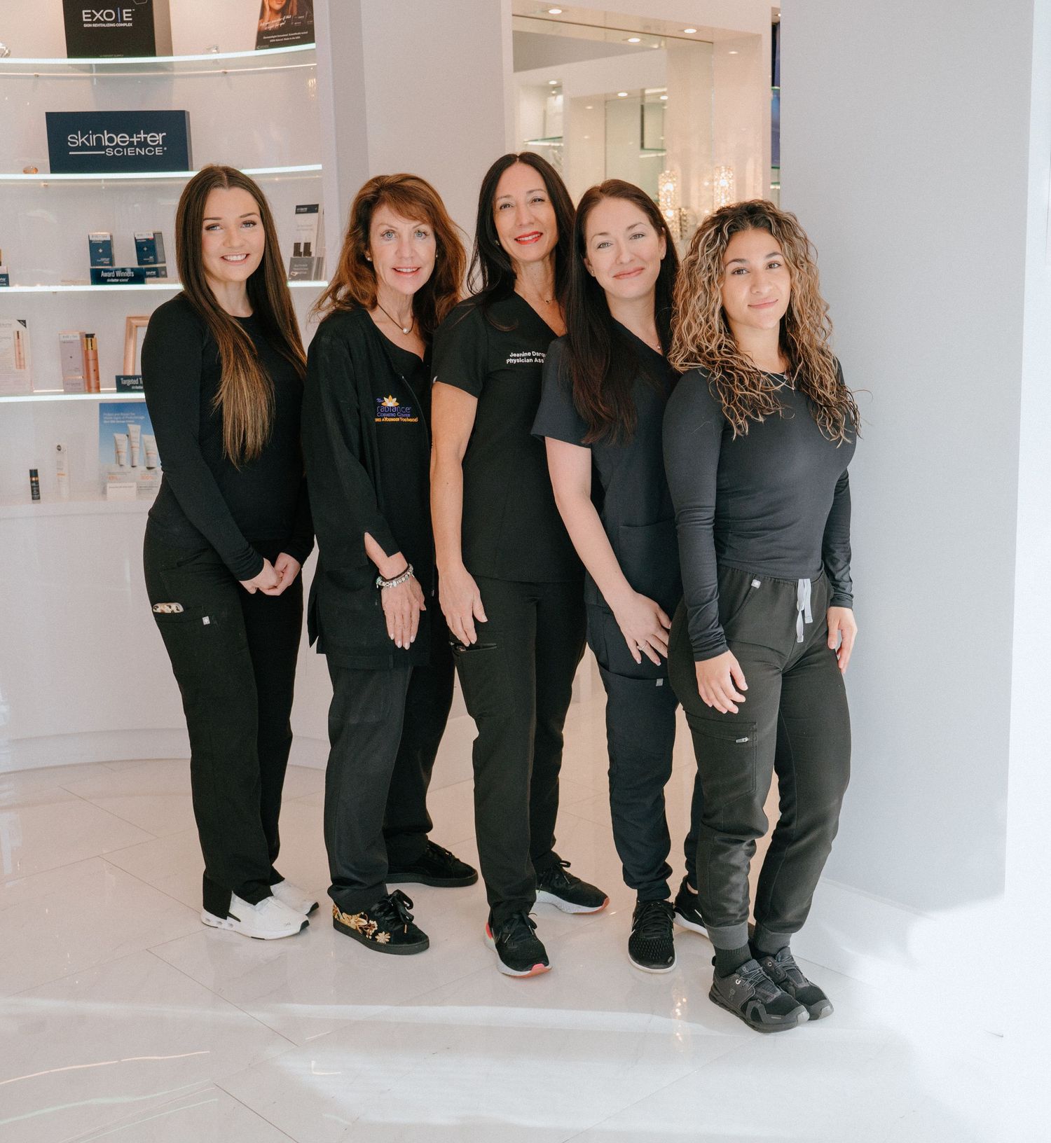Professional medical spa staff wearing black uniforms pose together in bright modern clinic setting.