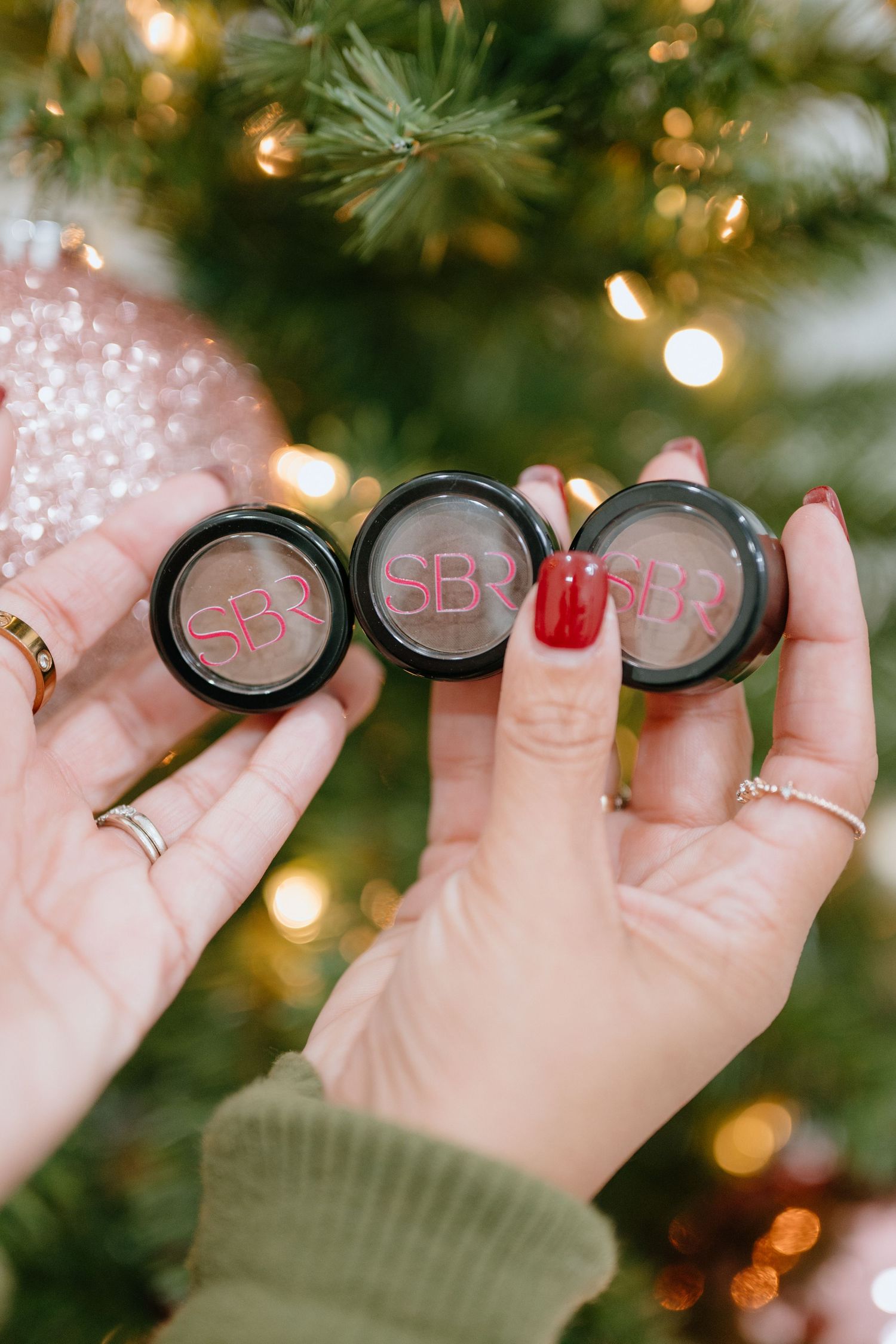 Hands displaying three makeup compacts against sparkly holiday background.