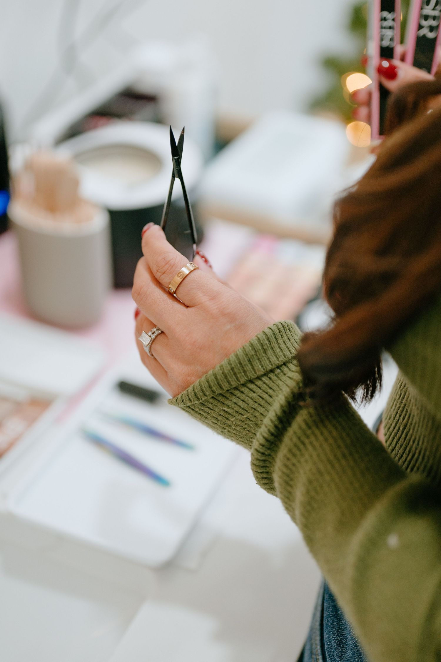 Hands wearing a green sweater holding small scissors with beauty products on the table.