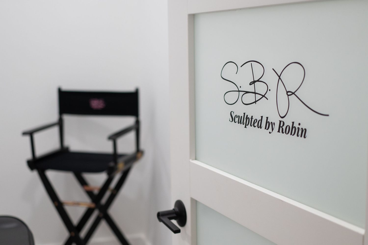 Director's chair and branded wall sign in a clean, minimalist beauty studio setting.