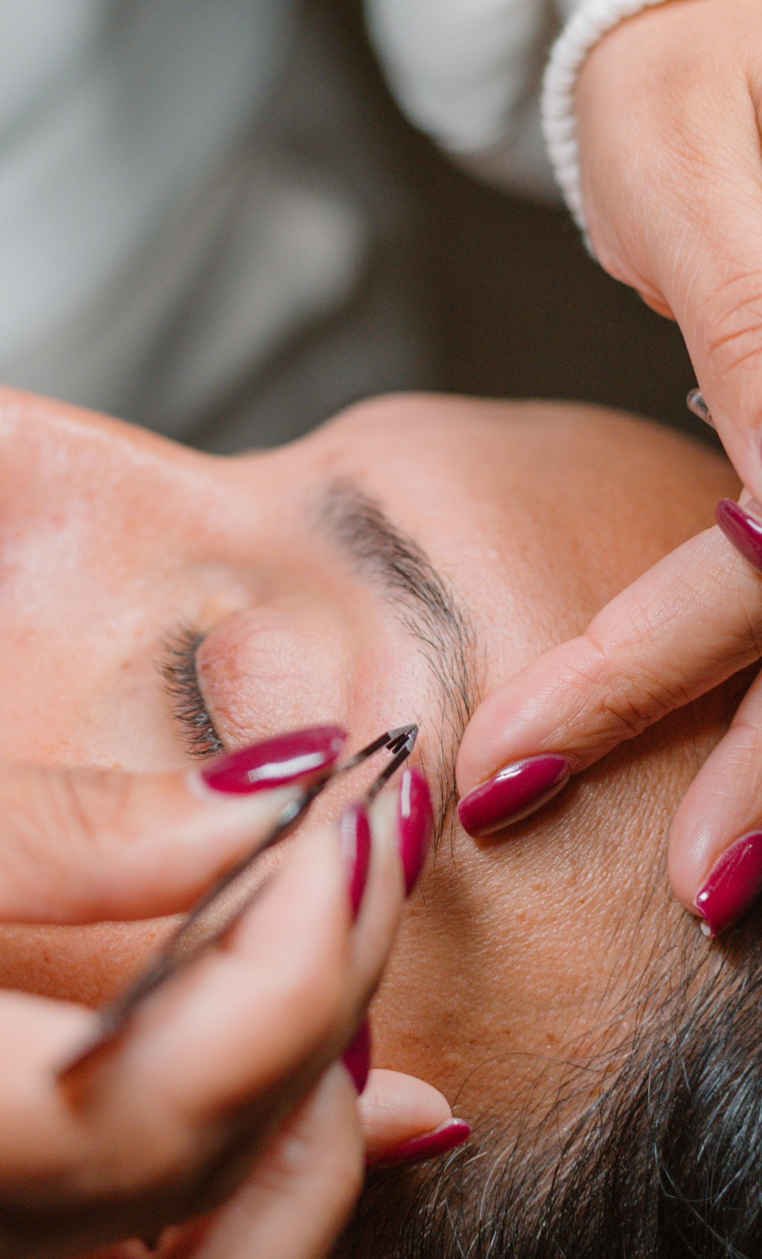 Professional eyebrow shaping session showing detailed precision work with red manicured nails.