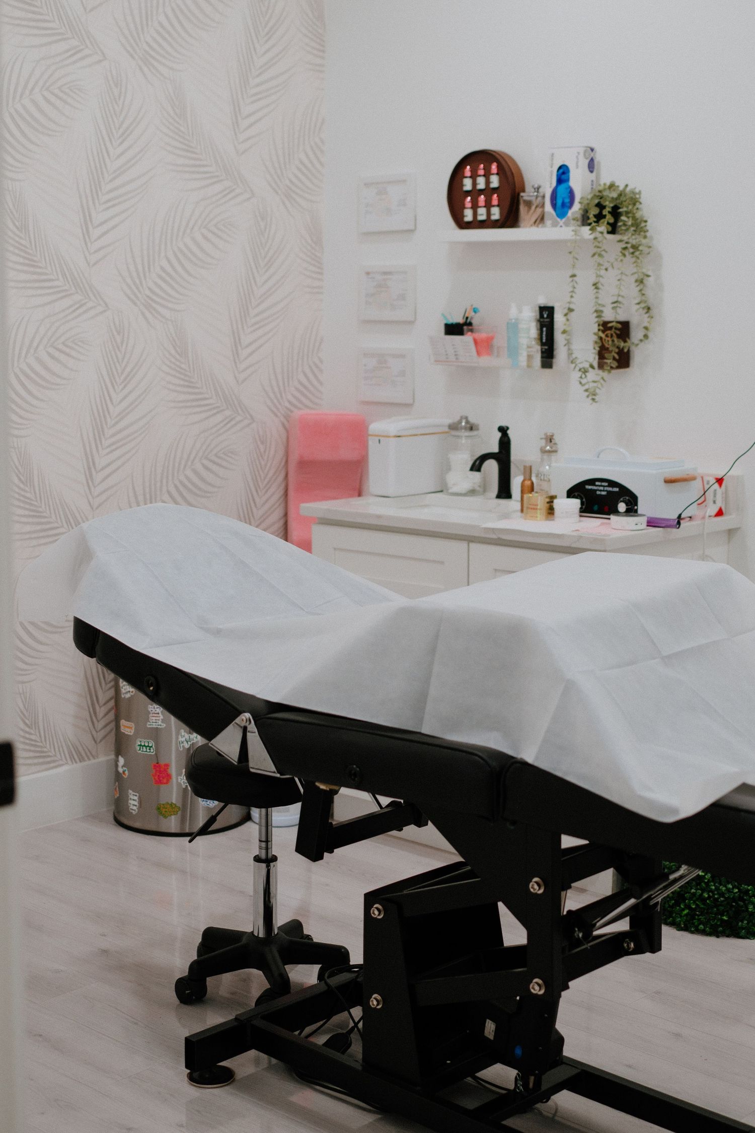 Professional spa treatment room with white massage table and modern decor featuring leaf-patterned wallpaper.
