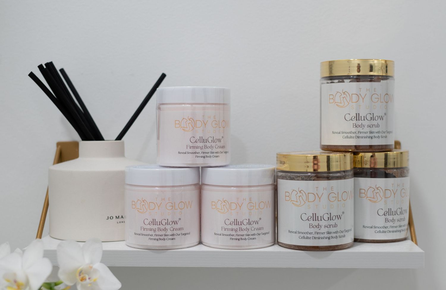 Collection of elegant white and gold beauty product jars displayed on shelf with decorative elements.