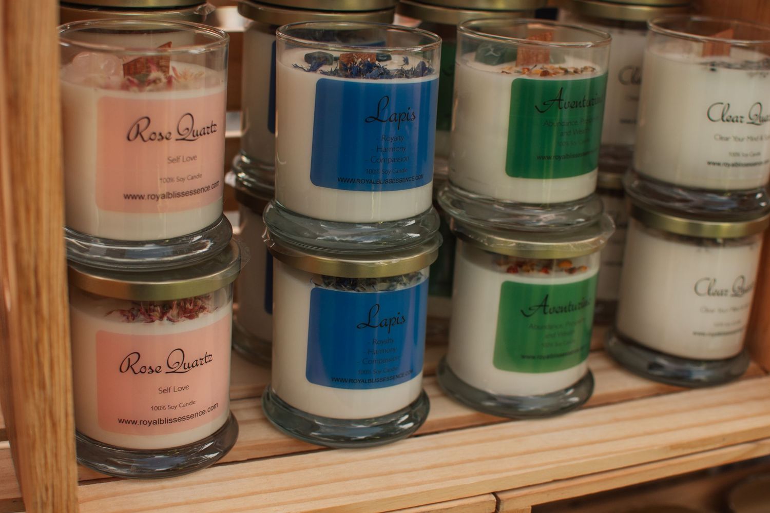 Assorted scented candles in glass jars arranged on wooden shelf.