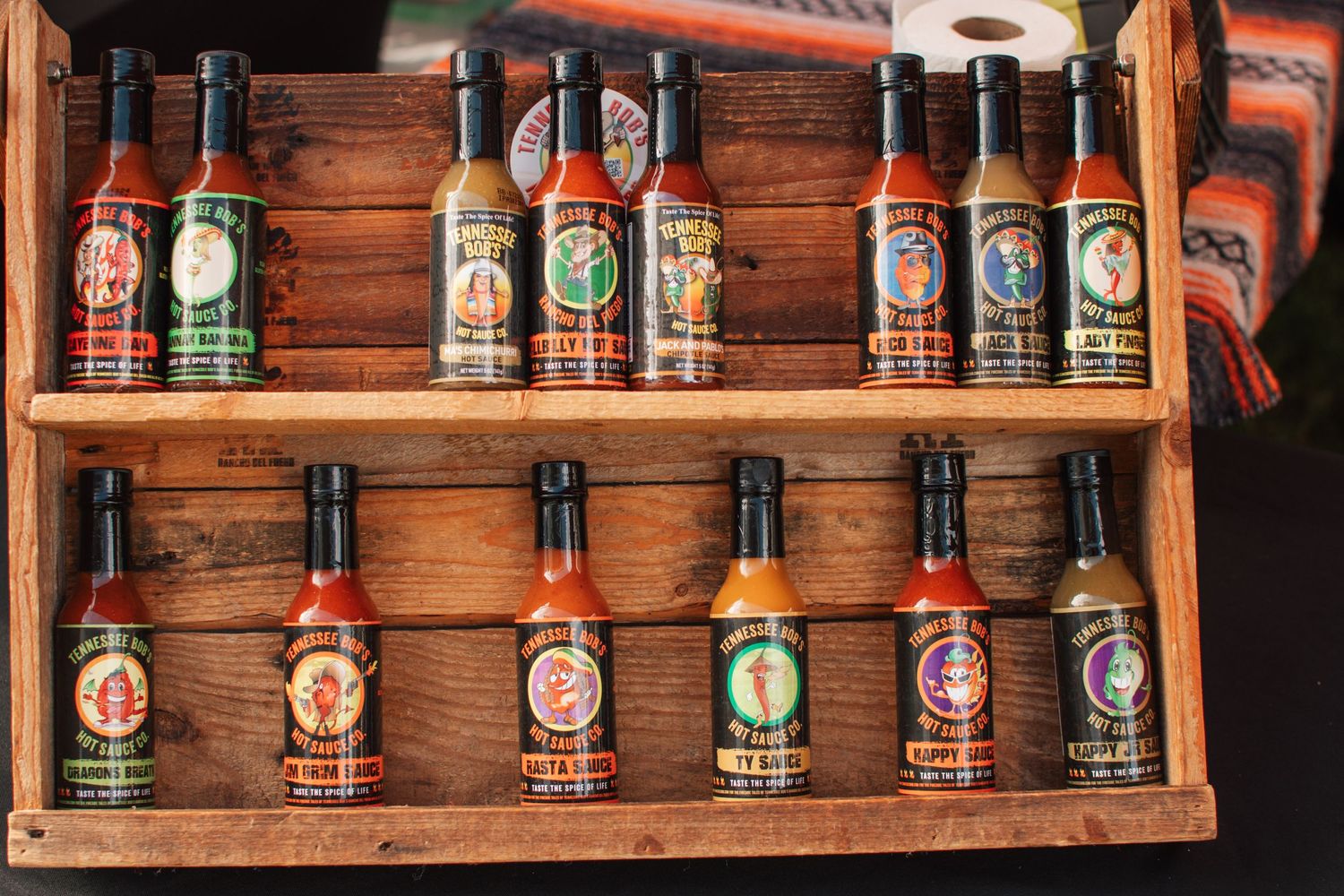Wooden shelf displaying collection of hot sauce bottles arranged in rows.
