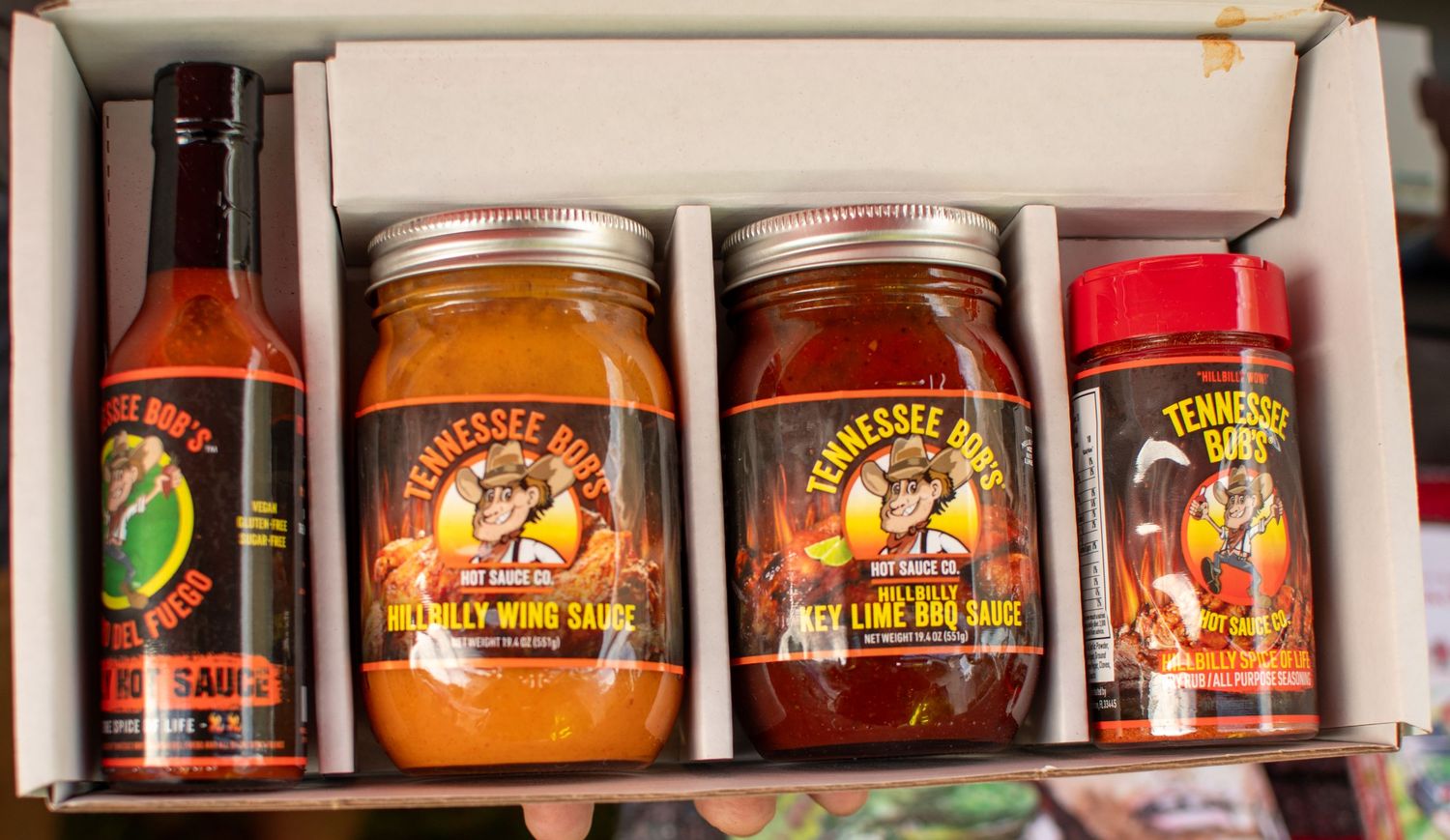 Collection of artisanal hot sauce and barbecue sauce bottles displayed in a wooden box.