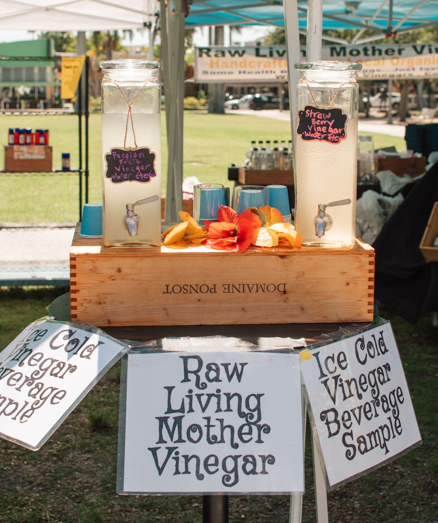 Wooden display stand featuring raw living vinegar products at an outdoor market.