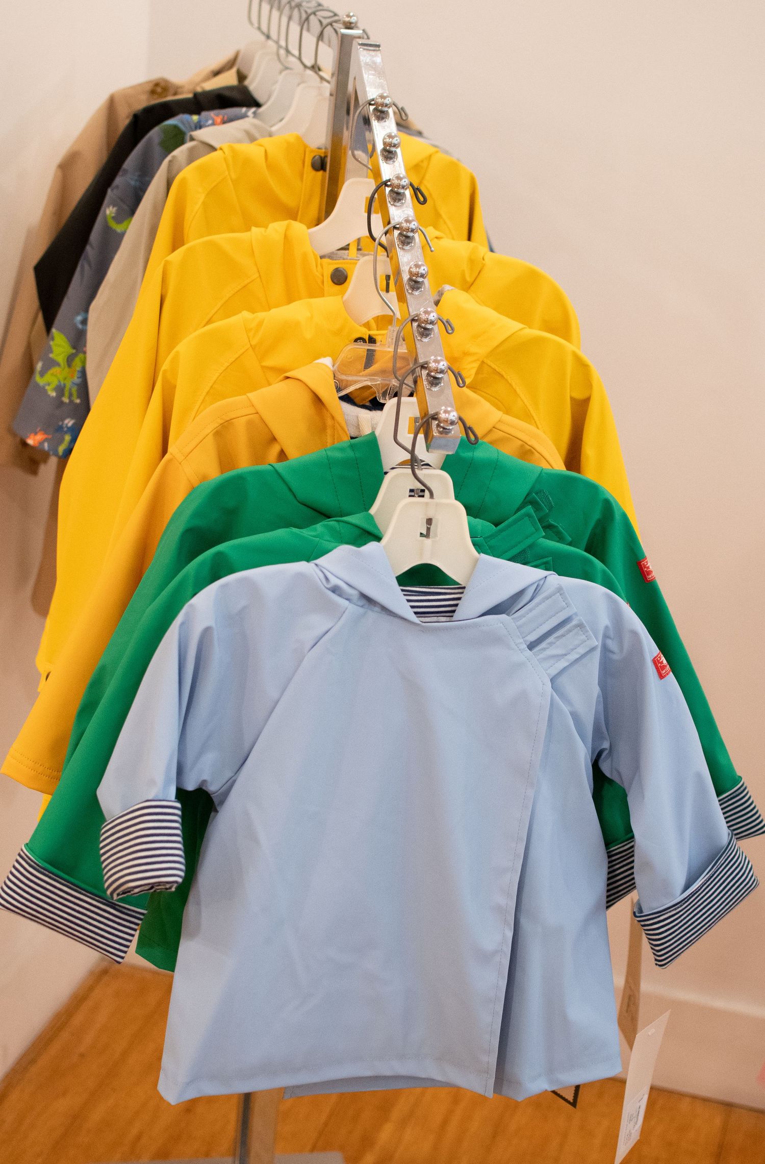 Row of children's shirts in yellow, green and blue hanging on retail display rack.