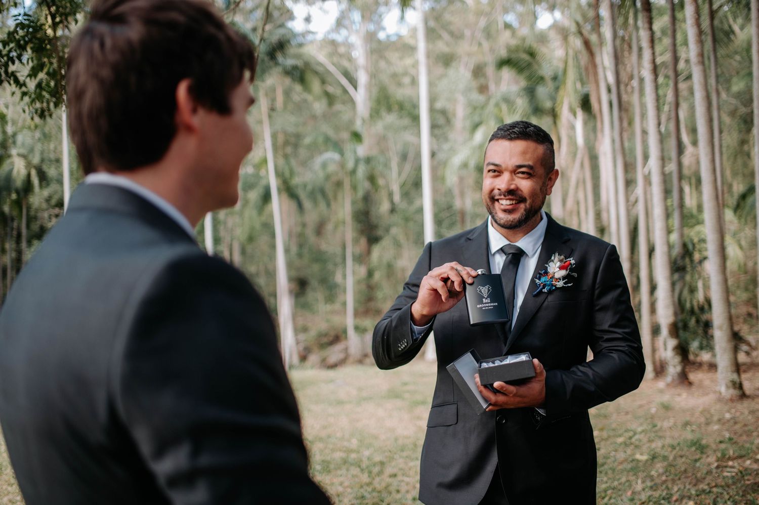 Two people in suits share a lighthearted moment in a eucalyptus grove.