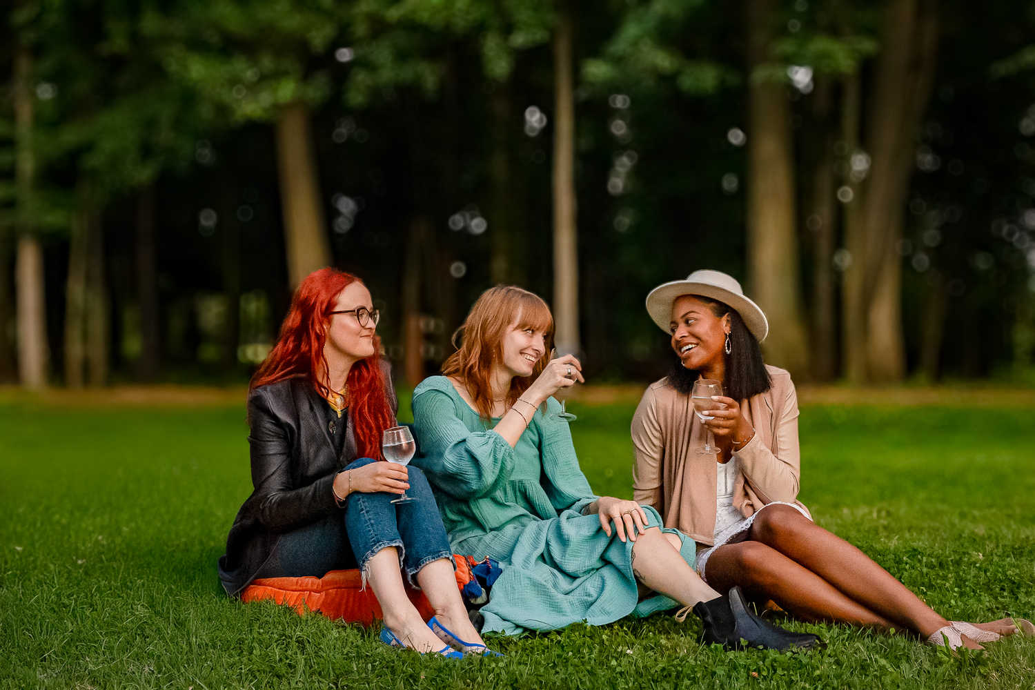 Group of friends enjoying drinks and conversation while sitting on grass in a park.