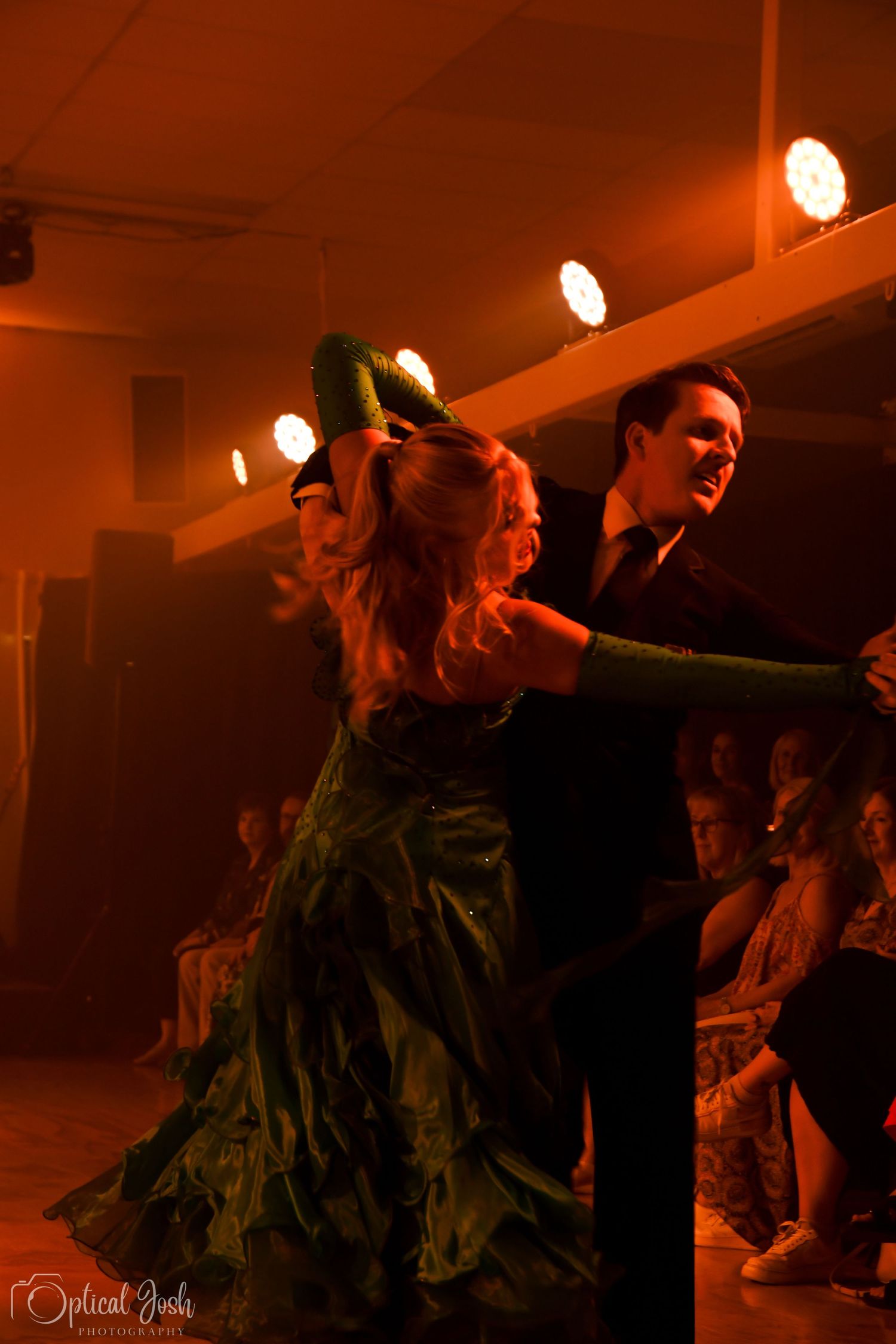 Dancers perform a dramatic ballroom dance routine in an atmospheric venue with orange lighting and a dark dress. (Optical Josh)