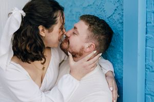 A tender romantic moment between a couple wearing white against a bright blue wall background.