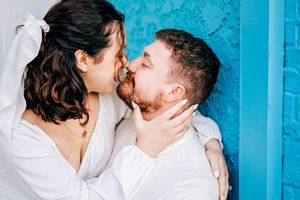 Two people share an intimate kiss in front of a bright turquoise painted wall during an outdoor photo session.