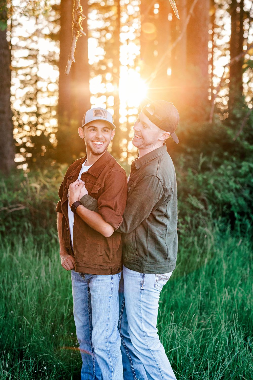 Two people share a joyful moment in casual attire against a sunlit forest backdrop during golden hour.
