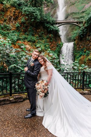 A couple in wedding attire poses together on a viewing deck at Multnomah Falls in Oregon's Columbia River Gorge.