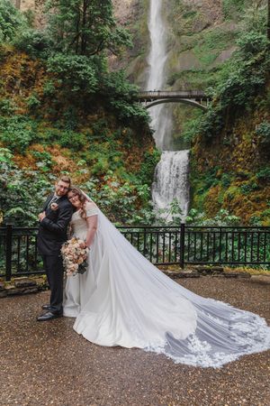 A beautiful wedding photo captured at Multnomah Falls in Oregon with a dramatic waterfall and bridge backdrop.