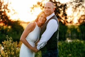 A couple embraces and smiles during a golden sunset photoshoot in a natural outdoor setting.