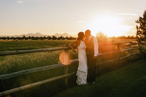 Two silhouettes hold hands in a sunset-lit wheat field with golden light streaming through the tall grass.