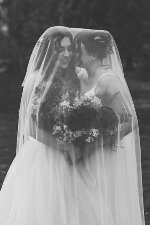 A romantic black and white wedding photo showing a couple sharing an intimate moment under a flowing veil.