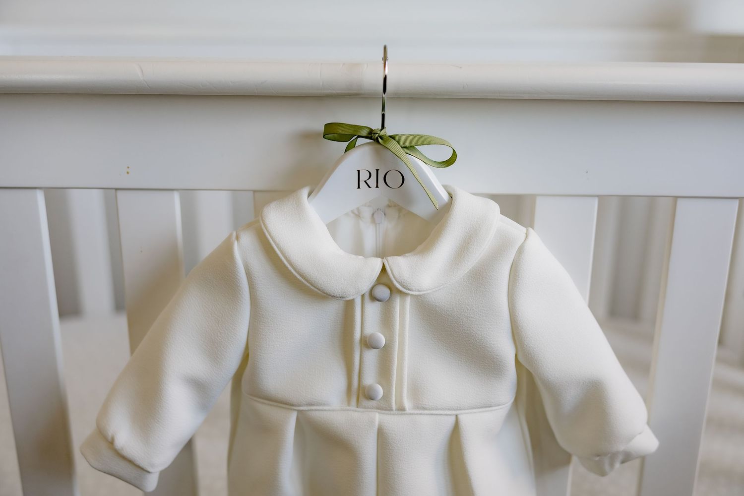 A white baby coat with peter pan collar hangs on a hanger.