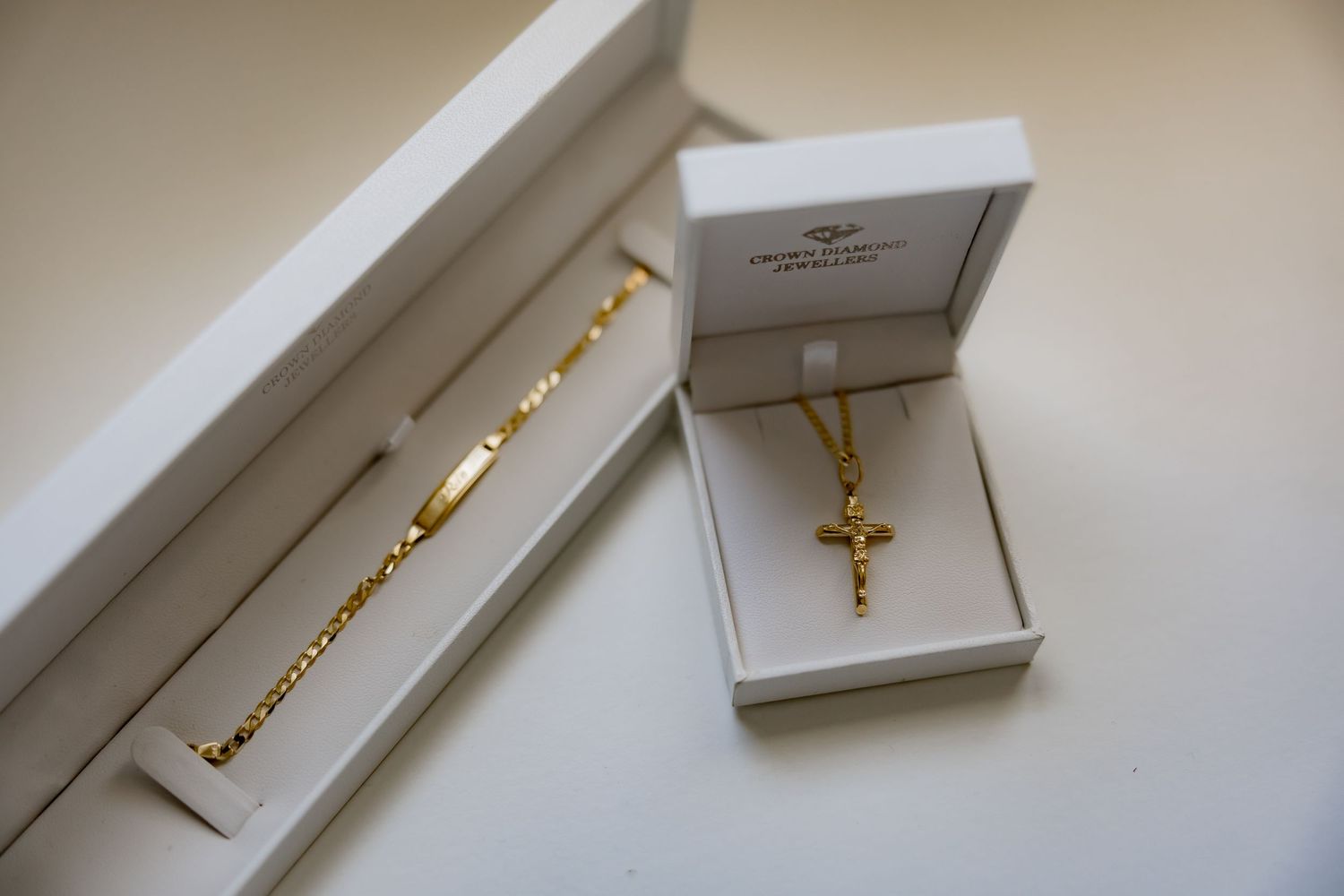 Gold jewelry pieces including a necklace and cross pendant displayed in white boxes.